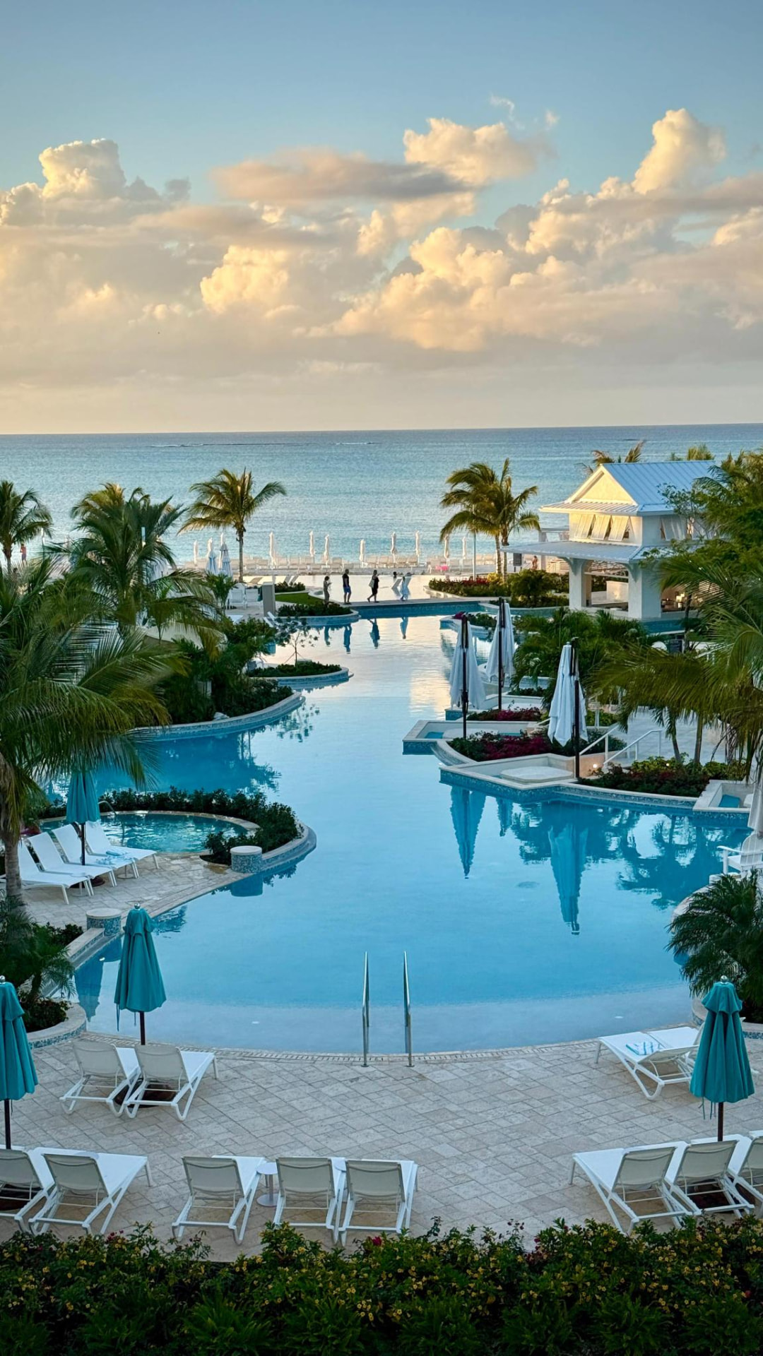 A resort pool glowing at sunset with the Caribbean sea beyond