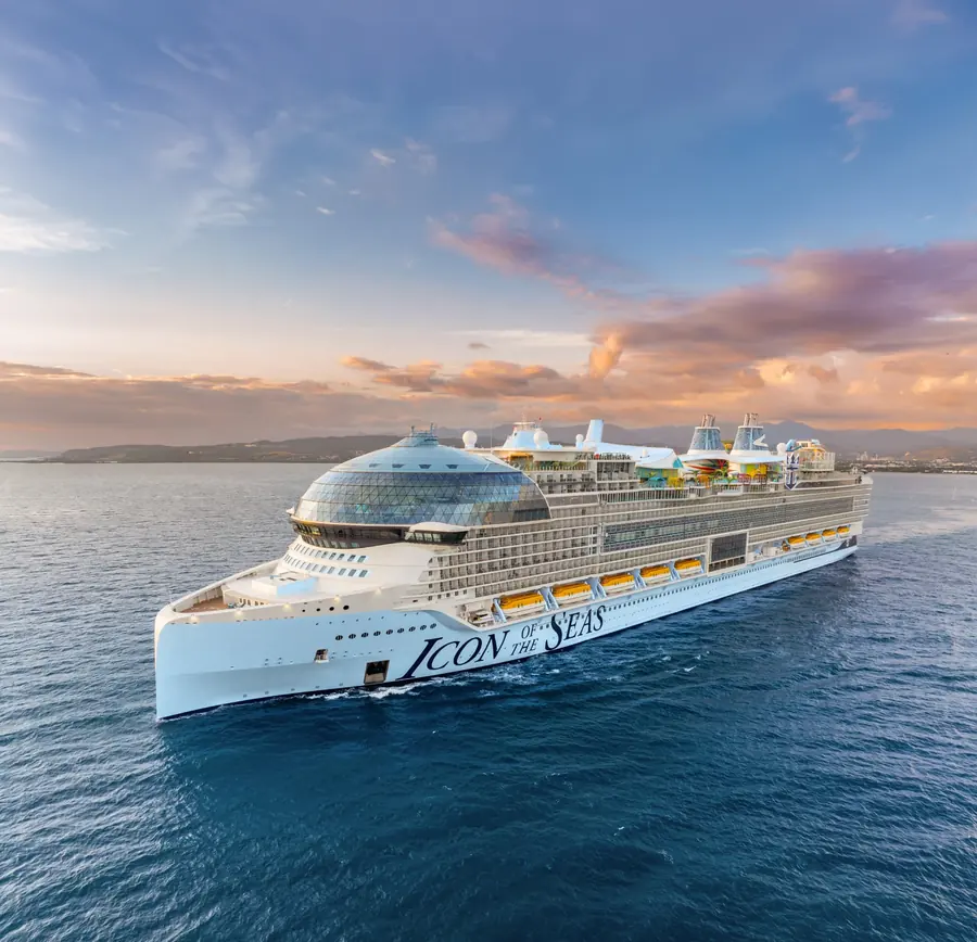 A cruise ship sailing at sunset off a mountainous coastline